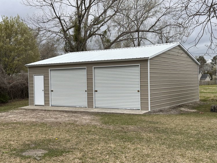 Prefab metal garage with two roll-up doors and white roof on concrete slab — metal garages Raleigh NC